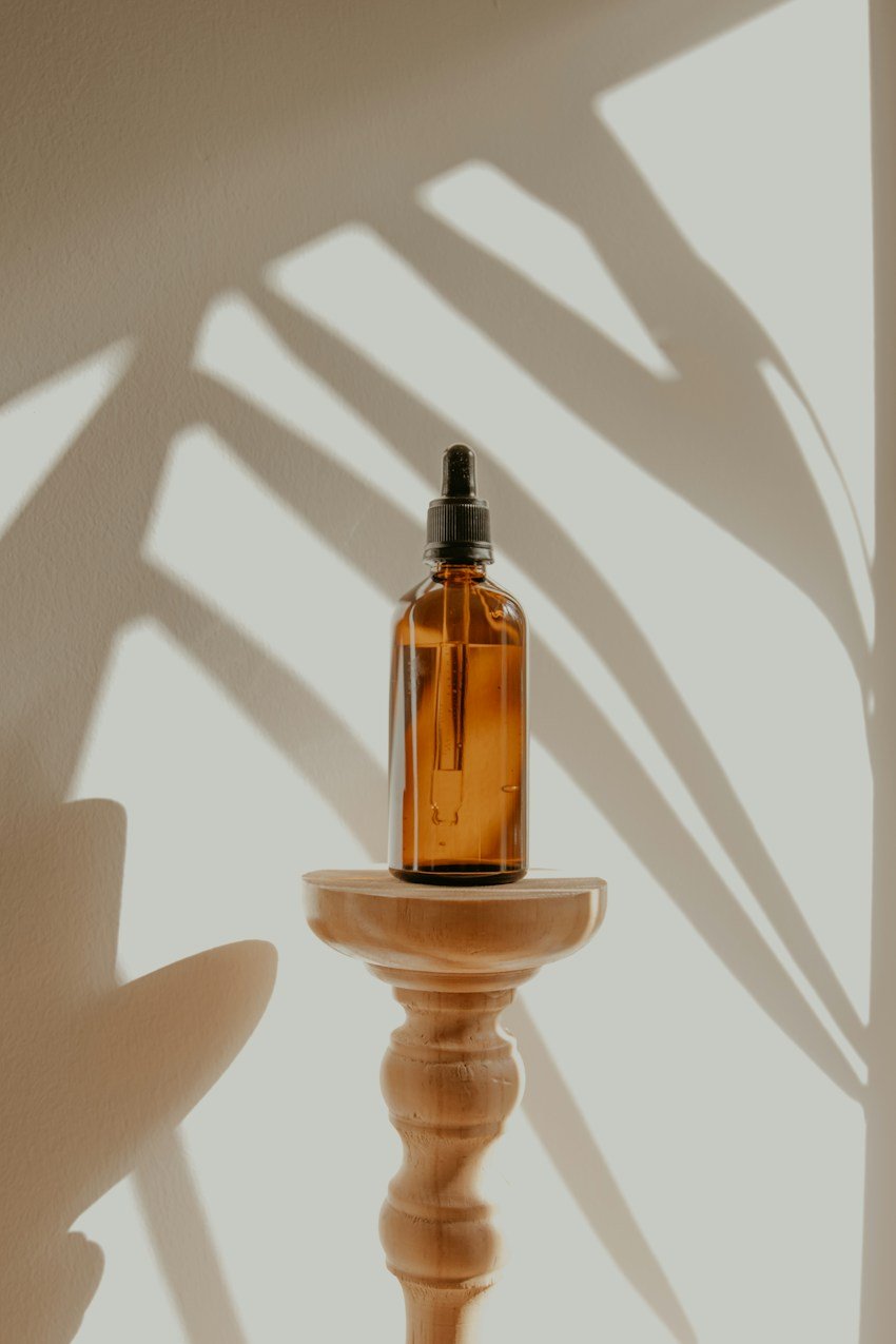 Amber essential oil dropper bottle in soft botanical shadows